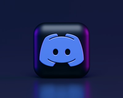 A 3D-style block with a blue logo in the center, set against a dark background. The logo resembles a game controller with two rounded edges and two circles on the front. The block has a subtle gradient, transitioning from dark to purple on its sides.